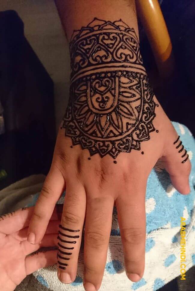 Arabic-style bold vine mehndi design on a man's backhand.